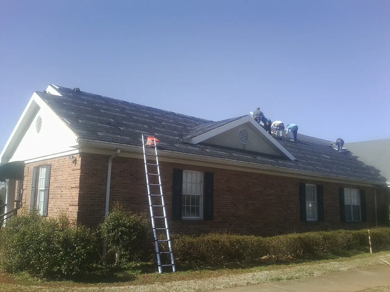 Crew tearing shingles off a brick ranch roof with a ladder set — Metal Roof Repair work by our crew in Monmouth
