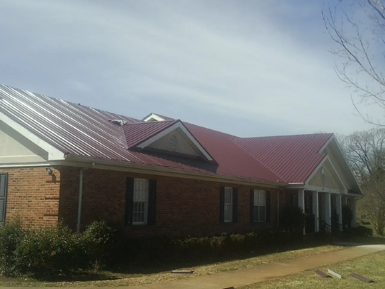 Red metal roof with gabled entries on a long brick building, from a Hail Damage Roof Repair job in Monmouth