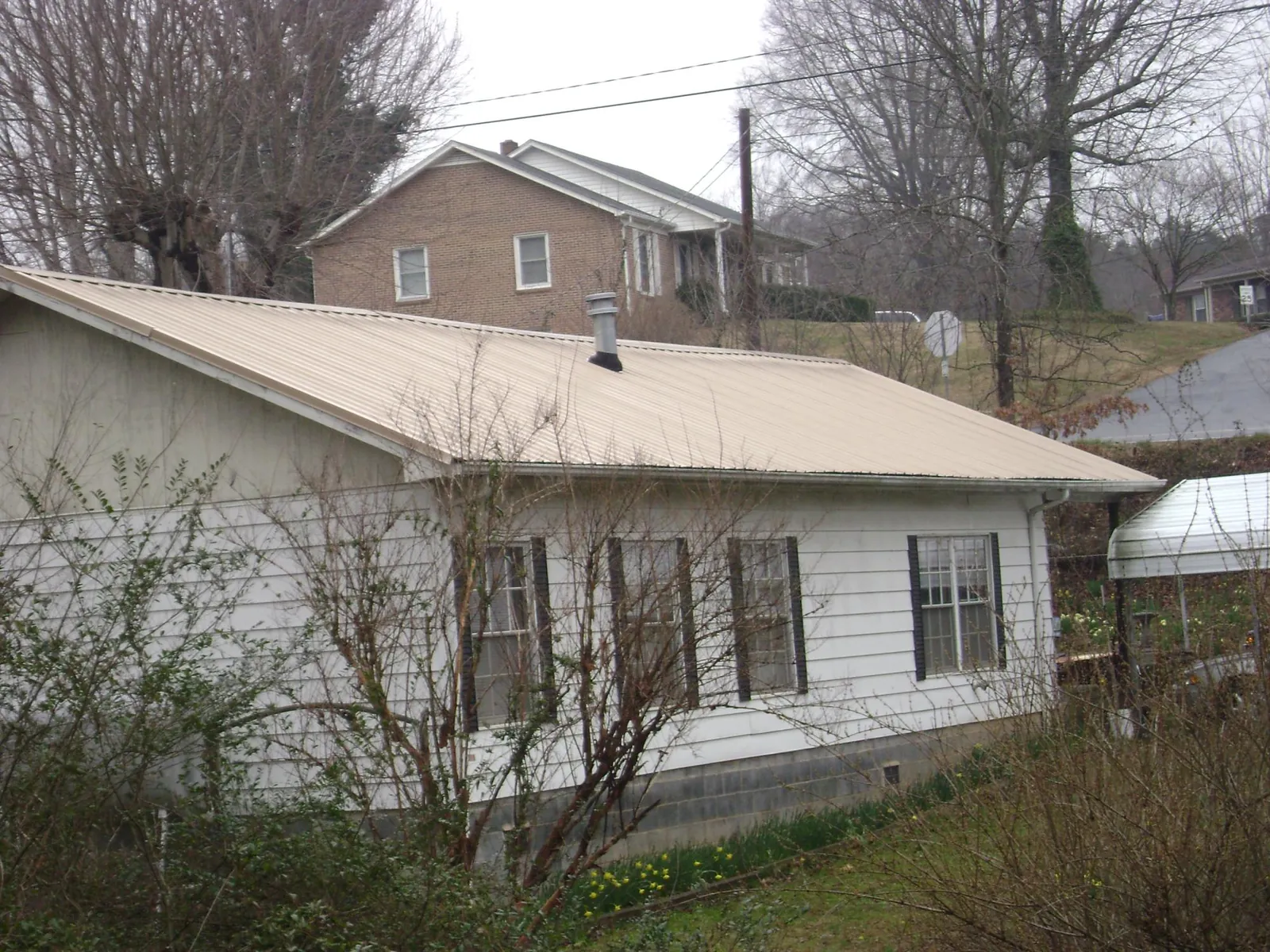 Tan metal roof on a white sided house set into a hillside — Commercial Roofing by Roofing Brothers in Monmouth