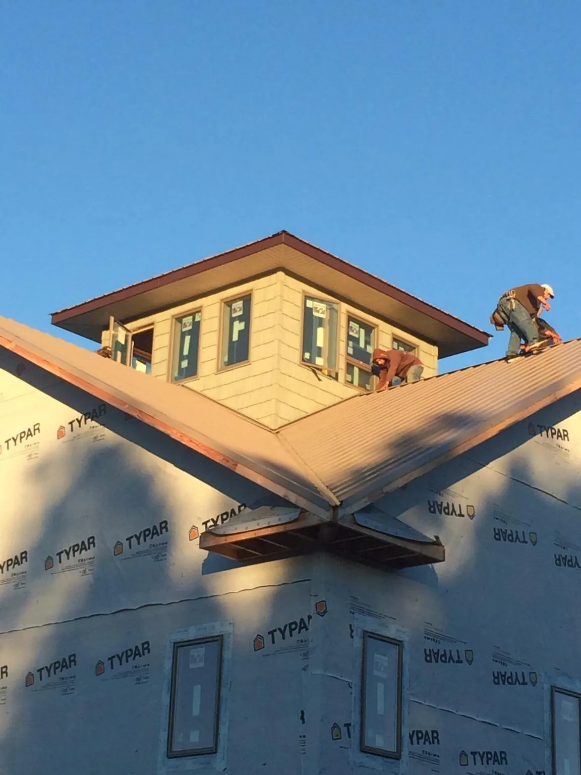 Roofers working around a rooftop cupola on a new metal roof at sunset in Monmouth